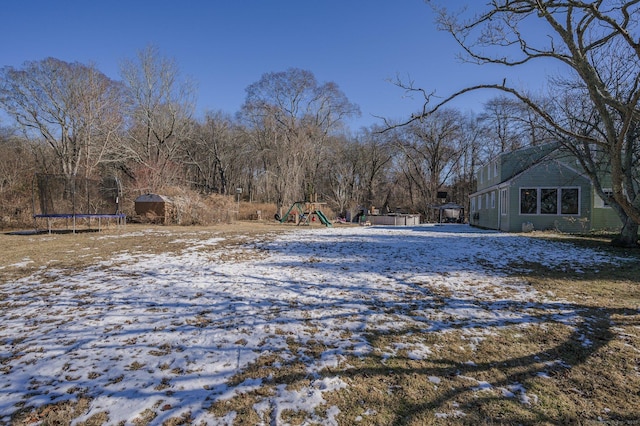 snowy yard featuring a trampoline and a playground