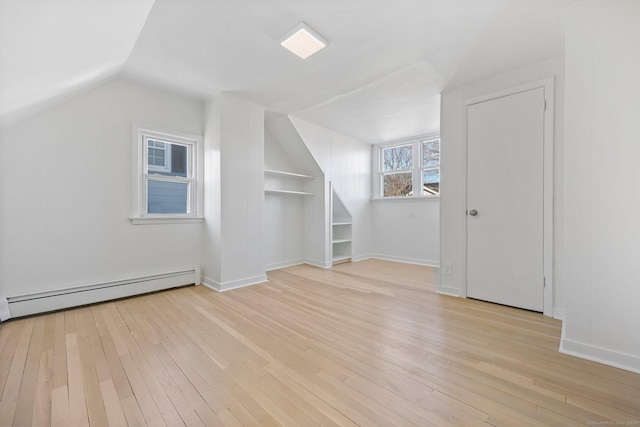 bonus room with vaulted ceiling, light wood-type flooring, baseboard heating, and built in shelves