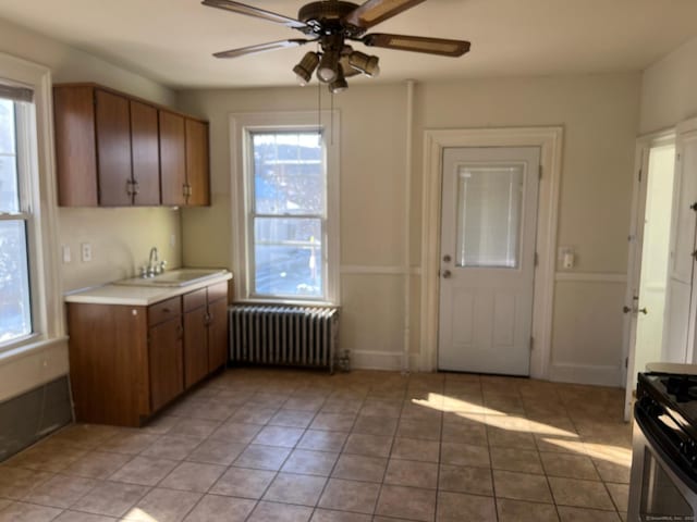 kitchen featuring radiator, stainless steel gas stove, sink, light tile patterned floors, and ceiling fan