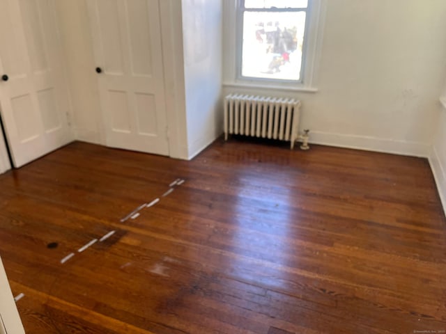 unfurnished bedroom with dark hardwood / wood-style flooring and radiator