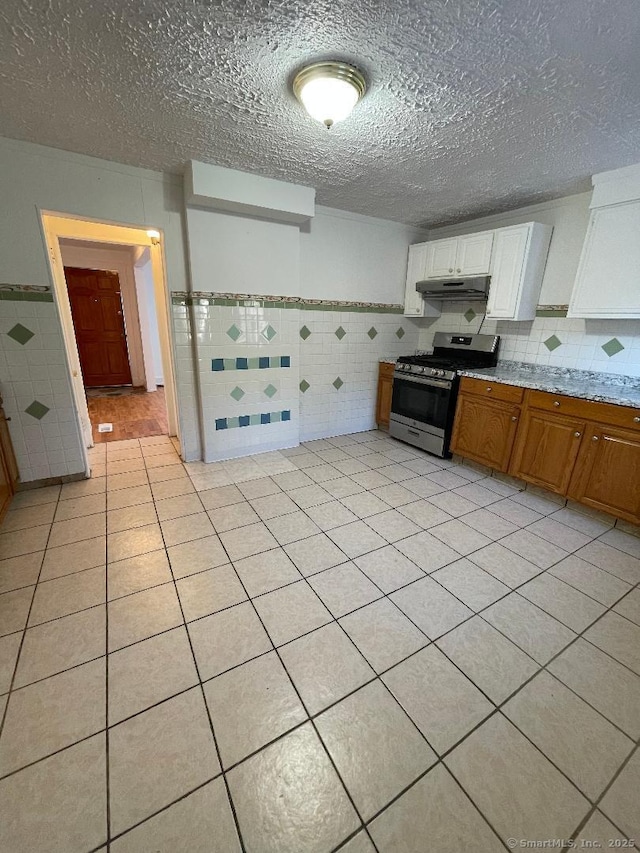 kitchen featuring stainless steel range with gas cooktop, light tile patterned floors, white cabinets, and tile walls