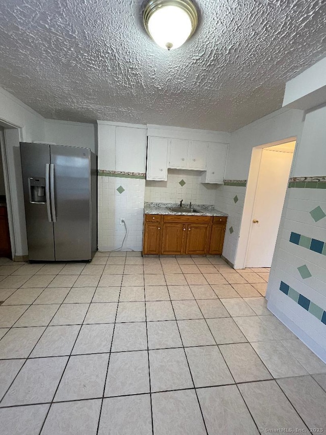 kitchen with light tile patterned floors, sink, white cabinetry, backsplash, and stainless steel fridge with ice dispenser