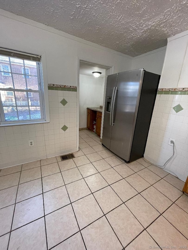 kitchen with tile walls, stainless steel fridge, a textured ceiling, and light tile patterned flooring