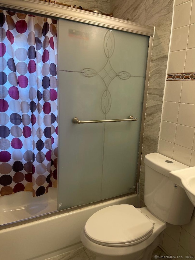 bathroom with bath / shower combo with glass door, tile walls, and toilet