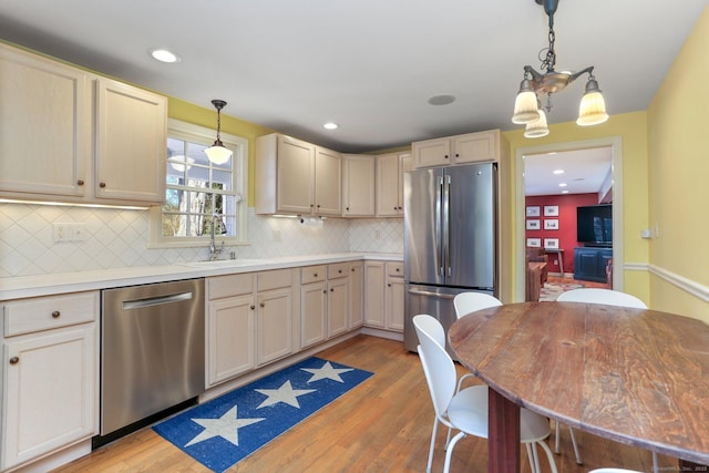 kitchen with sink, appliances with stainless steel finishes, decorative light fixtures, and light hardwood / wood-style floors