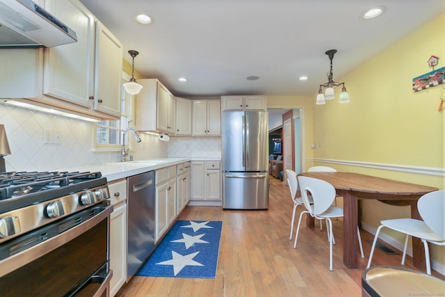 kitchen featuring hanging light fixtures, appliances with stainless steel finishes, sink, and exhaust hood