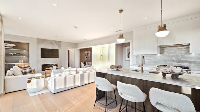 kitchen featuring pendant lighting, a fireplace, sink, backsplash, and white cabinets