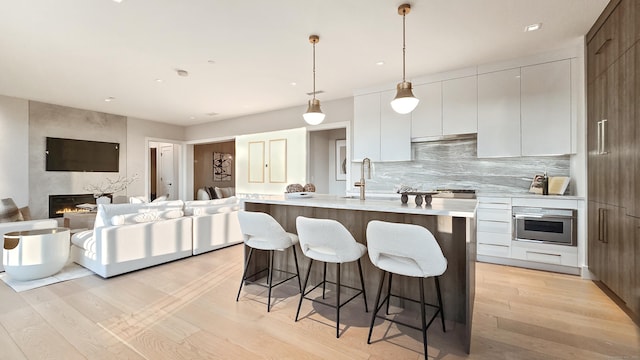 kitchen featuring decorative light fixtures, white cabinetry, an island with sink, a large fireplace, and stainless steel oven