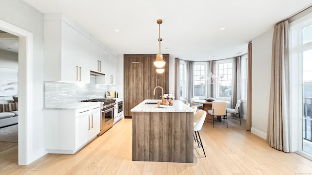 kitchen featuring sink, white cabinetry, high end range, decorative light fixtures, and a kitchen island with sink