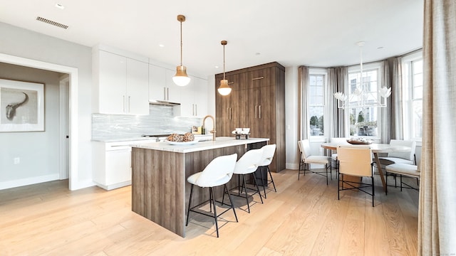 kitchen with decorative light fixtures, light hardwood / wood-style flooring, white cabinets, and a center island with sink