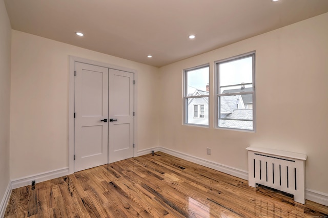 702 King St, Stratford, CT 06614 - unfurnished bedroom featuring radiator, wood finished floors, baseboards, recessed lighting, and a closet