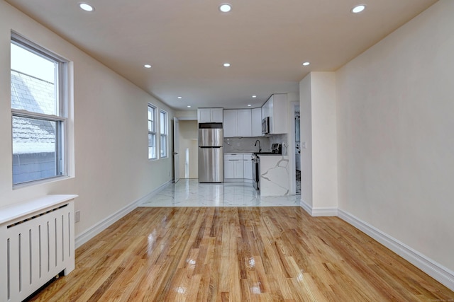 702 King St, Stratford, CT 06614 - unfurnished living room with radiator, baseboards, recessed lighting, light wood finished floors, and a sink
