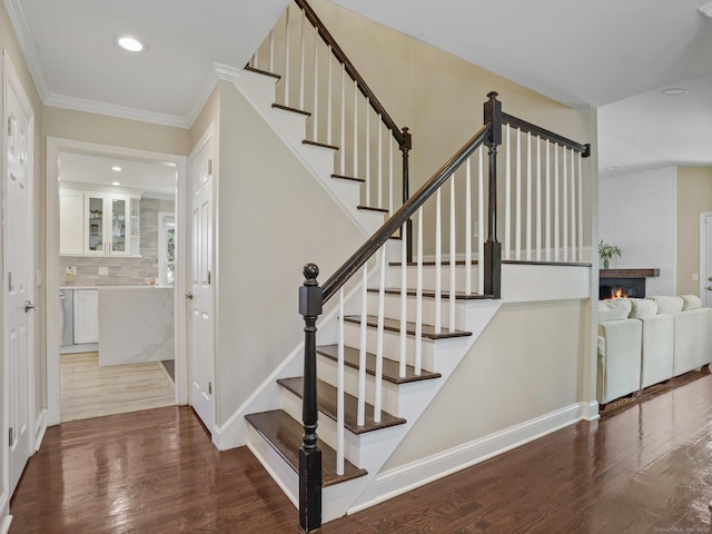 stairway featuring hardwood / wood-style flooring, ornamental molding, and a brick fireplace