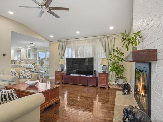 living room featuring dark hardwood / wood-style flooring, lofted ceiling, ceiling fan, and a fireplace