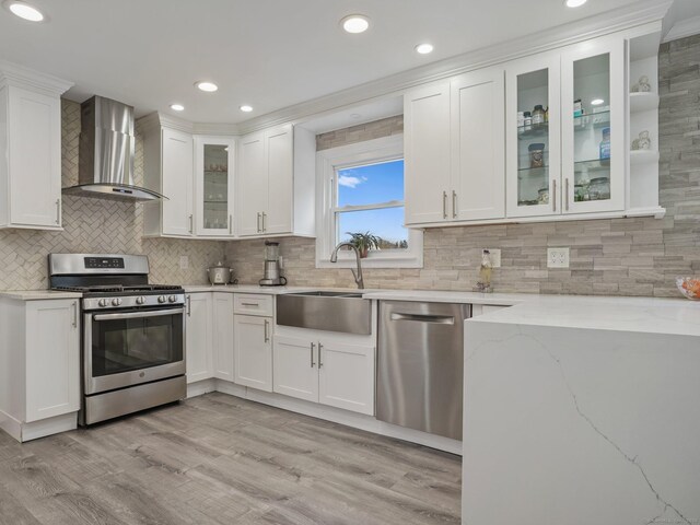 kitchen featuring wall chimney range hood, stainless steel appliances, and white cabinets