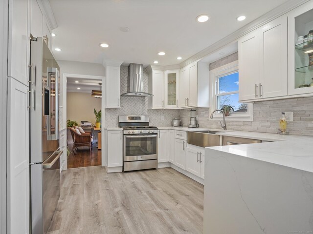 kitchen featuring white cabinetry, sink, stainless steel appliances, light stone countertops, and wall chimney range hood