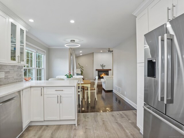 kitchen featuring white cabinetry, stainless steel appliances, a brick fireplace, and tasteful backsplash