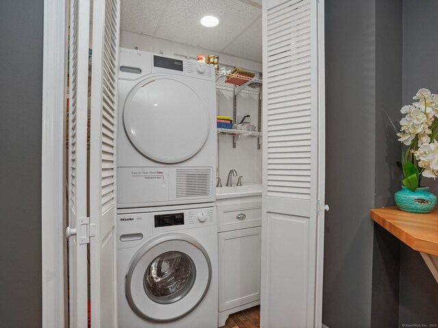 washroom with cabinets, stacked washer and clothes dryer, and sink