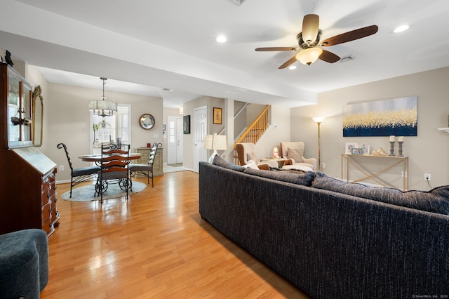 living room with ceiling fan with notable chandelier and light hardwood / wood-style flooring