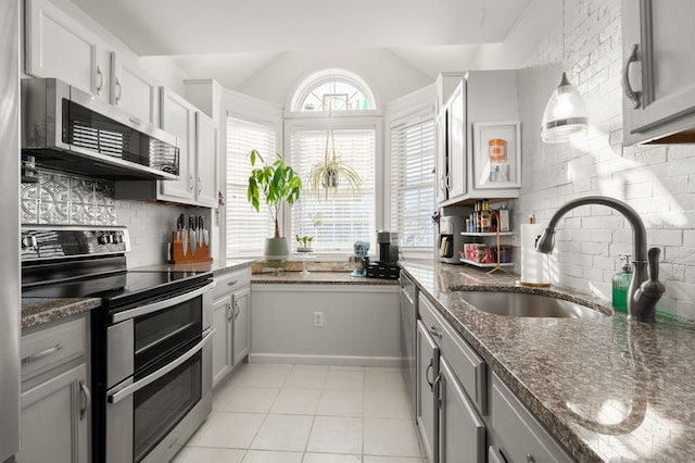 kitchen with sink, appliances with stainless steel finishes, gray cabinetry, decorative light fixtures, and dark stone counters