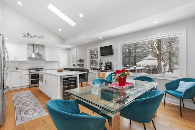 kitchen featuring a kitchen island, white cabinetry, beverage cooler, stainless steel appliances, and wall chimney range hood