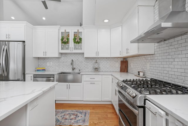 kitchen with sink, white cabinetry, appliances with stainless steel finishes, light stone countertops, and wall chimney range hood