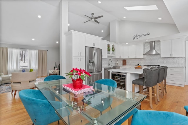 dining area with ceiling fan, a skylight, high vaulted ceiling, wine cooler, and light hardwood / wood-style floors