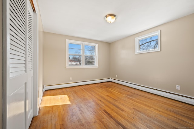 unfurnished bedroom featuring baseboard heating, multiple windows, and light wood-type flooring