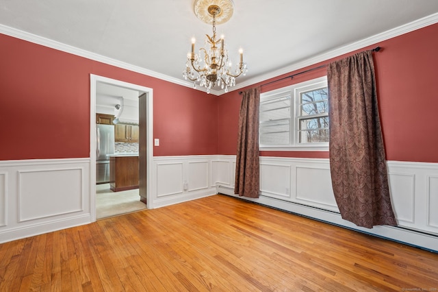 empty room featuring baseboard heating, ornamental molding, light hardwood / wood-style flooring, and a notable chandelier