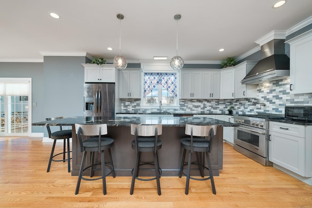 kitchen with appliances with stainless steel finishes, a center island, pendant lighting, and wall chimney exhaust hood