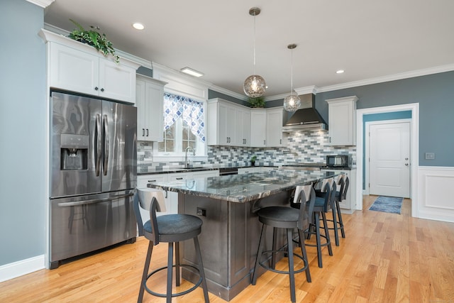 kitchen with wall chimney exhaust hood, stainless steel fridge with ice dispenser, a kitchen breakfast bar, a kitchen island, and pendant lighting