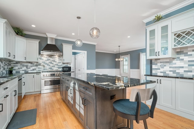 kitchen featuring pendant lighting, stainless steel stove, white cabinetry, a center island, and wall chimney range hood