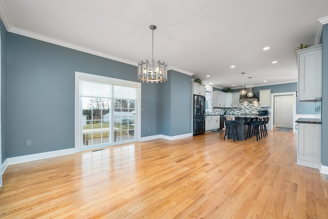 kitchen with a breakfast bar, black fridge with ice dispenser, a center island, hanging light fixtures, and wall chimney range hood