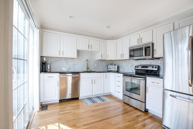 kitchen with dark countertops, appliances with stainless steel finishes, light wood-style floors, white cabinetry, and a sink