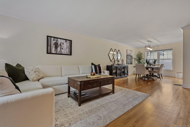 living room featuring baseboards, ornamental molding, light wood-type flooring, and a notable chandelier