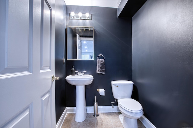 half bath with baseboards, toilet, and tile patterned floors