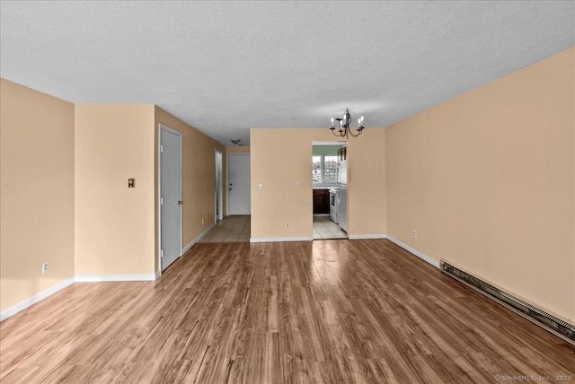 unfurnished living room with light hardwood / wood-style flooring, a textured ceiling, a baseboard radiator, and a chandelier