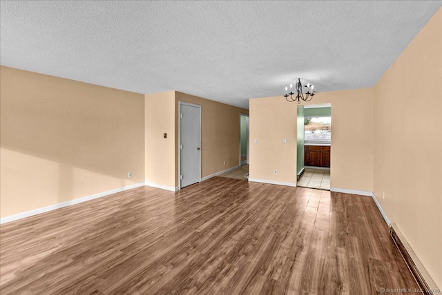 empty room featuring baseboard heating, a chandelier, light hardwood / wood-style floors, and a textured ceiling