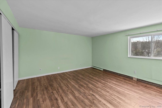 unfurnished bedroom featuring hardwood / wood-style flooring, a baseboard heating unit, and a closet