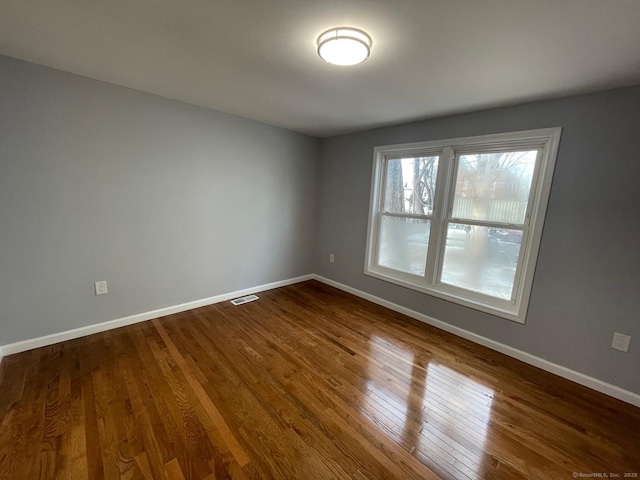 unfurnished room with visible vents, dark wood finished floors, and baseboards