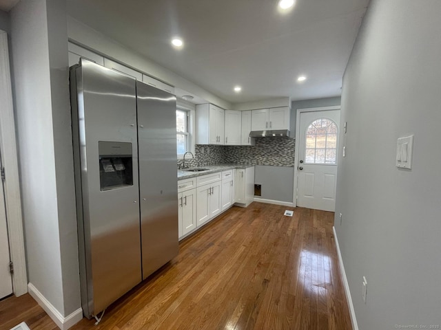 kitchen with decorative backsplash, wood finished floors, under cabinet range hood, white cabinetry, and a sink