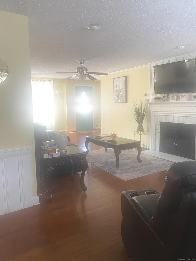 living room featuring a brick fireplace, hardwood / wood-style flooring, a textured ceiling, and ceiling fan