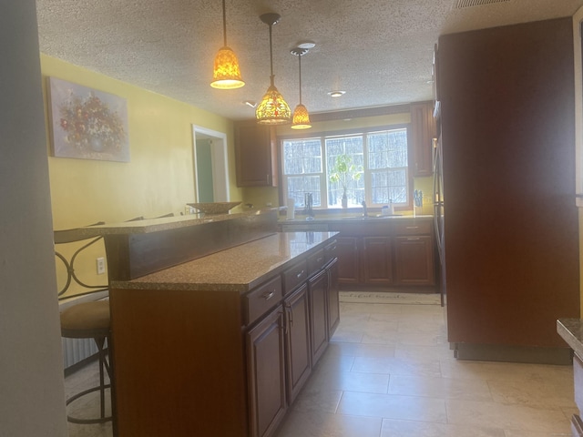 kitchen featuring hanging light fixtures, a breakfast bar area, kitchen peninsula, and a textured ceiling