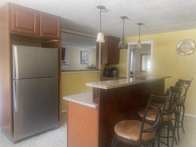 kitchen featuring stainless steel refrigerator, a breakfast bar, hanging light fixtures, a textured ceiling, and kitchen peninsula