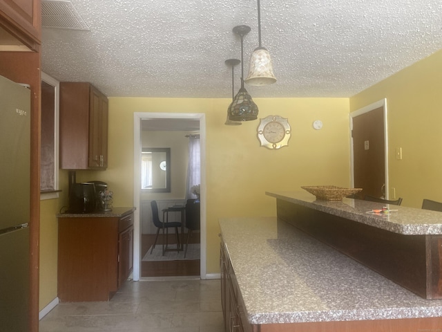 kitchen featuring light tile patterned flooring, fridge, a textured ceiling, and decorative light fixtures