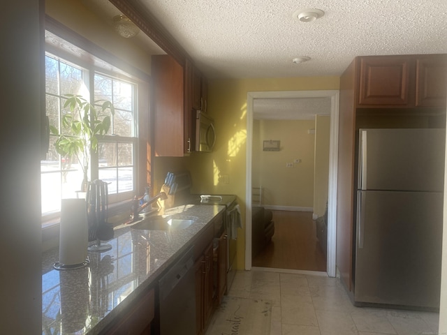 kitchen featuring light stone counters, stainless steel appliances, sink, and a textured ceiling