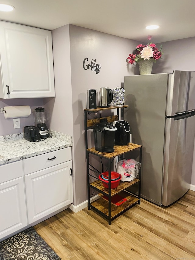 kitchen with white cabinets, stainless steel fridge, light stone counters, and light hardwood / wood-style flooring