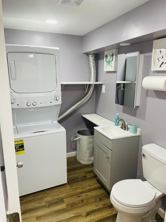 bathroom with hardwood / wood-style flooring, stacked washer and clothes dryer, toilet, and vanity