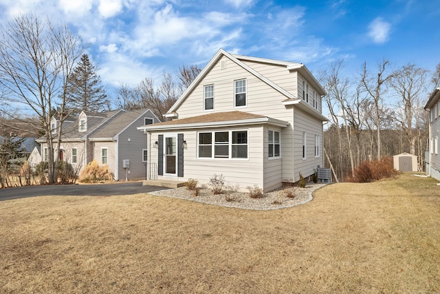 rear view of property featuring central AC, a storage unit, and a lawn