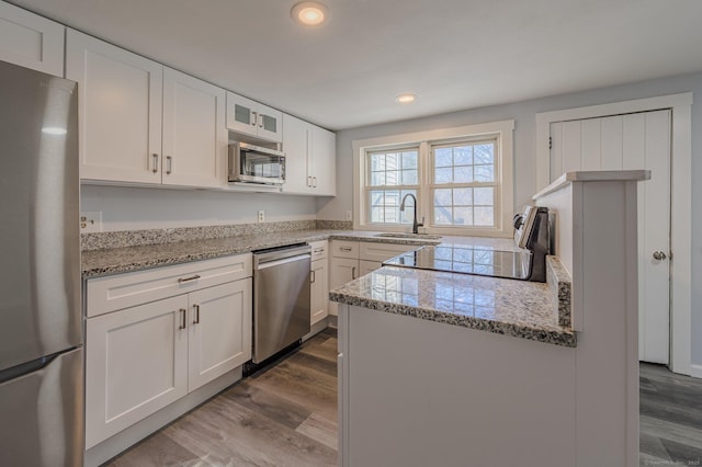 kitchen featuring sink, white cabinets, hardwood / wood-style flooring, light stone counters, and stainless steel appliances